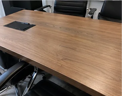 Meeting table with a walnut-effect film finish on the top and edge, black leather chairs around it and a cable port in the surface